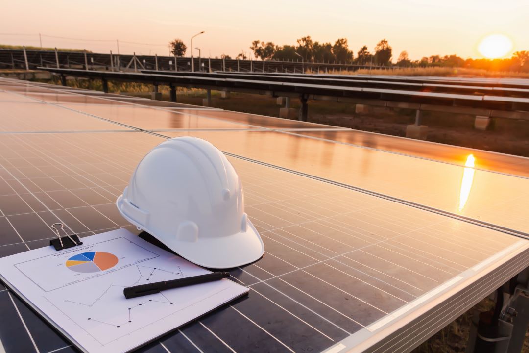 A helmet lies on a solarpanel with paper and a pen during sunset