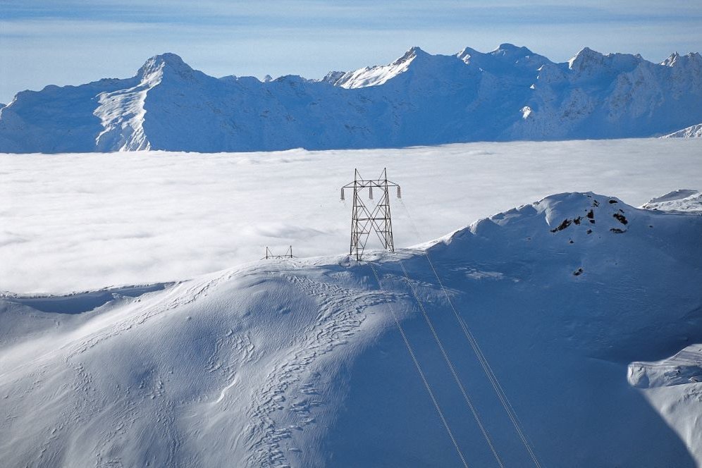A wide shot of a mountainrange and in the middle is a electricity pole