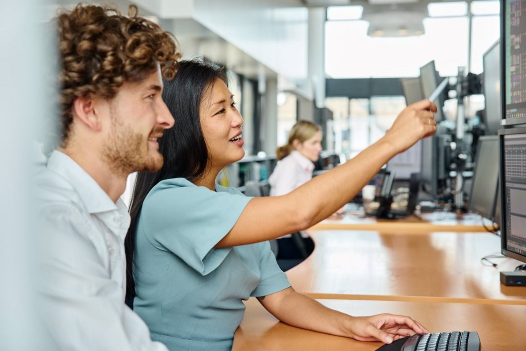 Two people sitting at a desk while they point at the screen