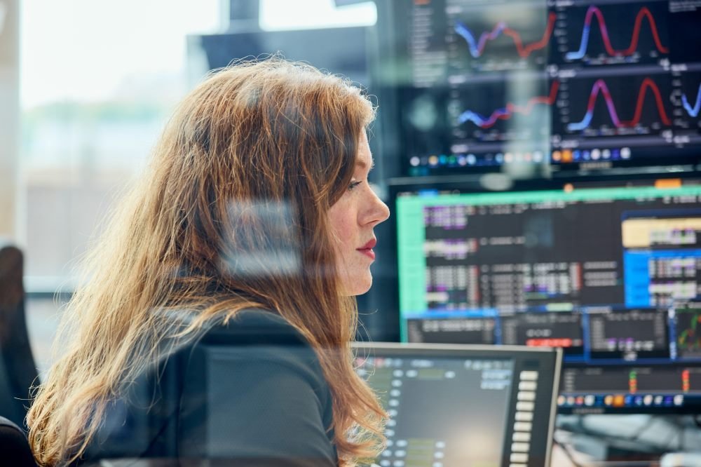 A trader sits at her desk and looks at screens