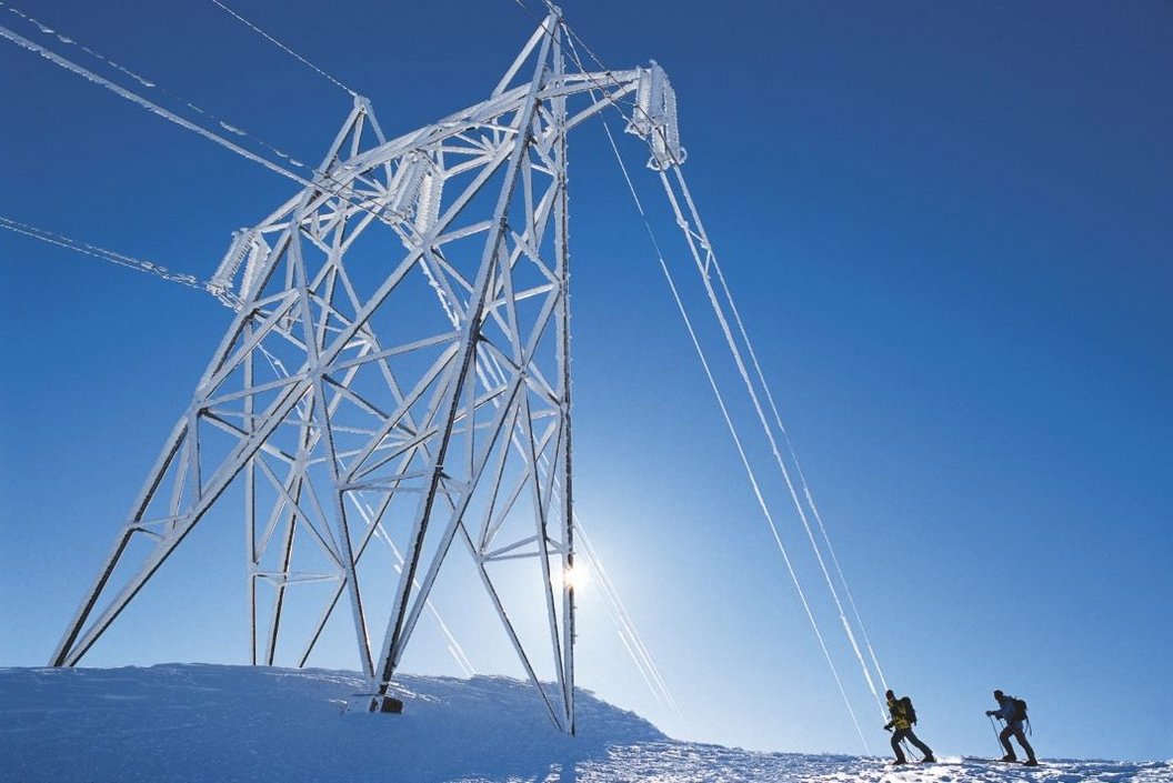 Electricity Pole in snow A big electricity pole is coverd in snow while to hikers are to its right