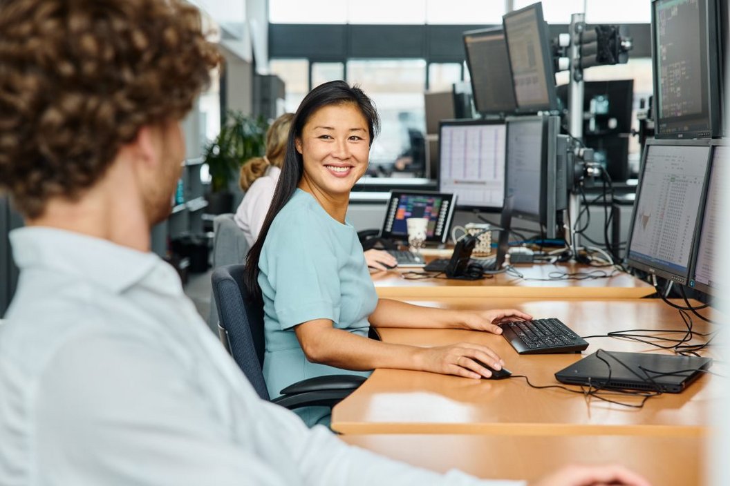 People talking on desk 2 People talking to each other on a desk with a lots of screen. The woman is facing the camera while the man is turned away.